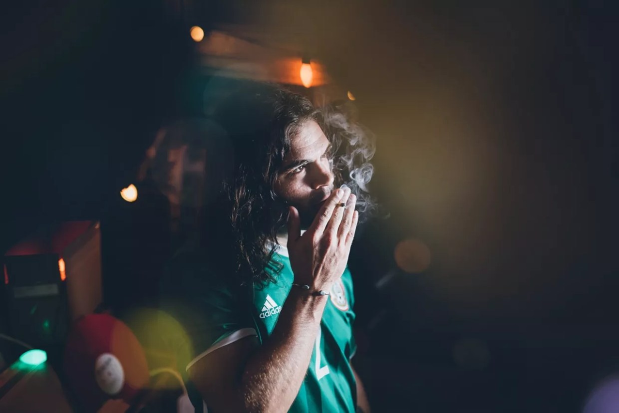 Man in soccer jersey with long hair smokes marijuana