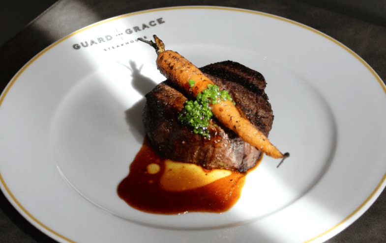 a steak with carrots on a white plate.