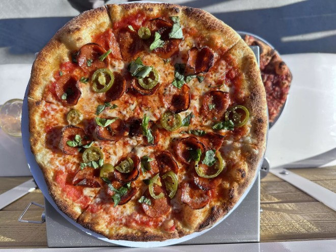 a pizza topped with with pepperoni, jalapeno and resh sliced garlic