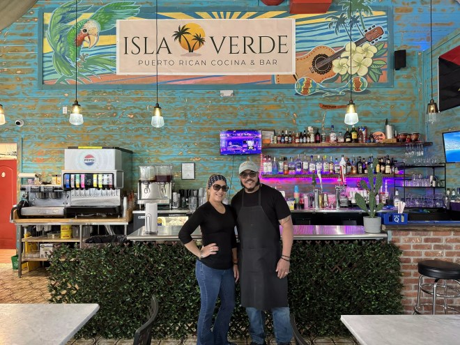 a woman and man posting in front of an "isla verde" sign