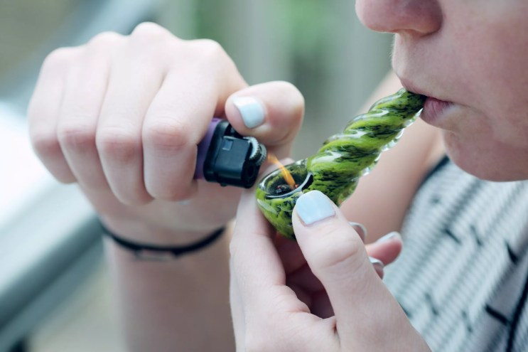 Woman smokes bowl of weed out of green pipe