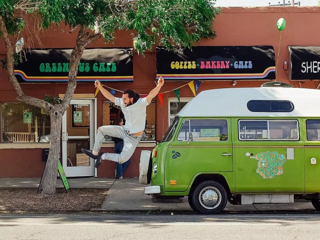 a man jumping in the air next to a vintage green bus