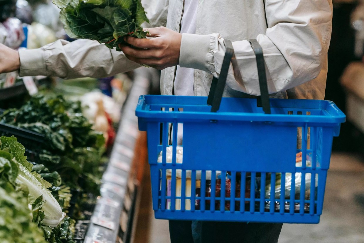 A man carries a blue hand-held grocery basket while shopping.