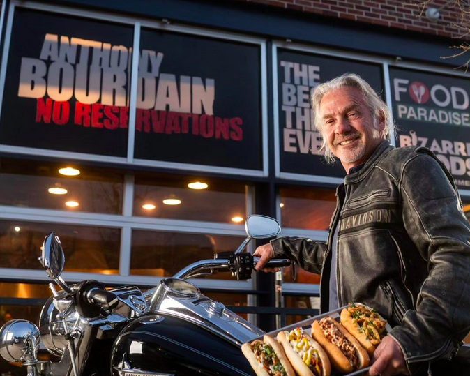 man standing next to a motorcycle holding a tray of hot dogs