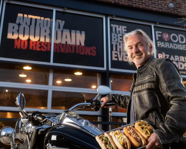 man standing next to a motorcycle holding a tray of hot dogs