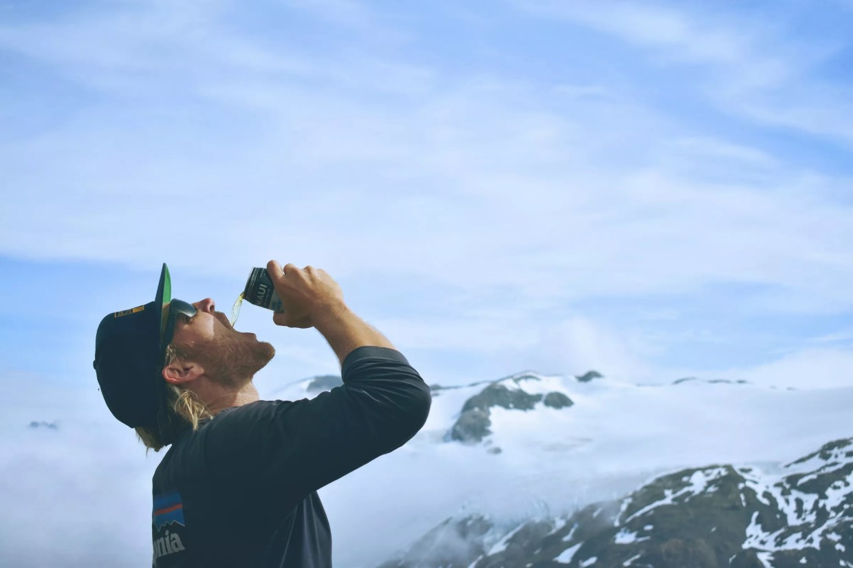 Man drinks beer on top of mountain