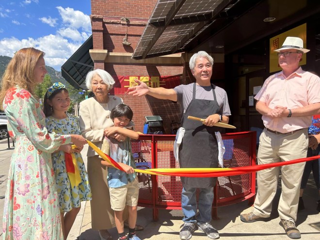 man in an apron standing with family and cutting a ribbon
