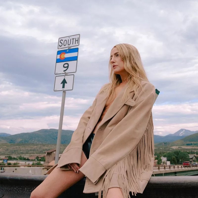 woman in buckskin jacket by highway sign