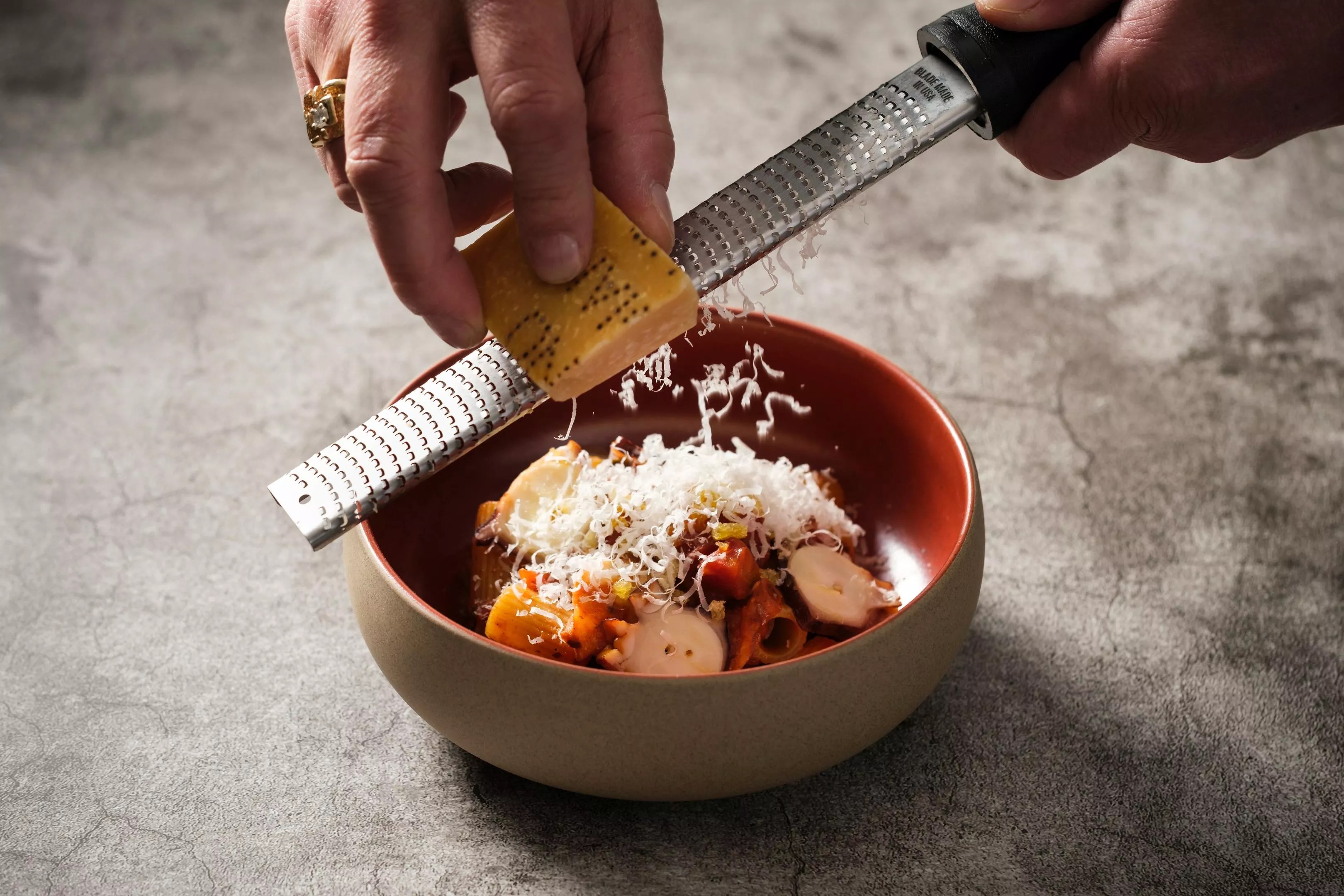 a hand grating parmesan over a bowl of pasta