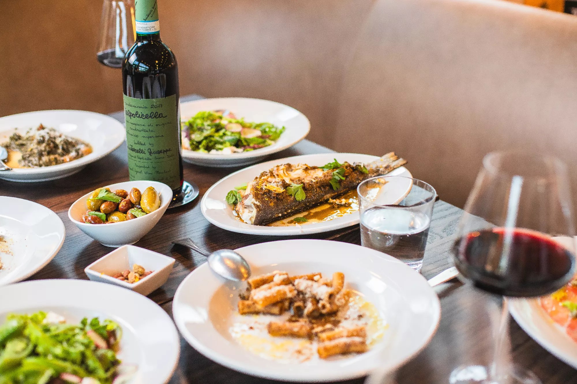 various foods on white plates set on a table with a bottle of wine
