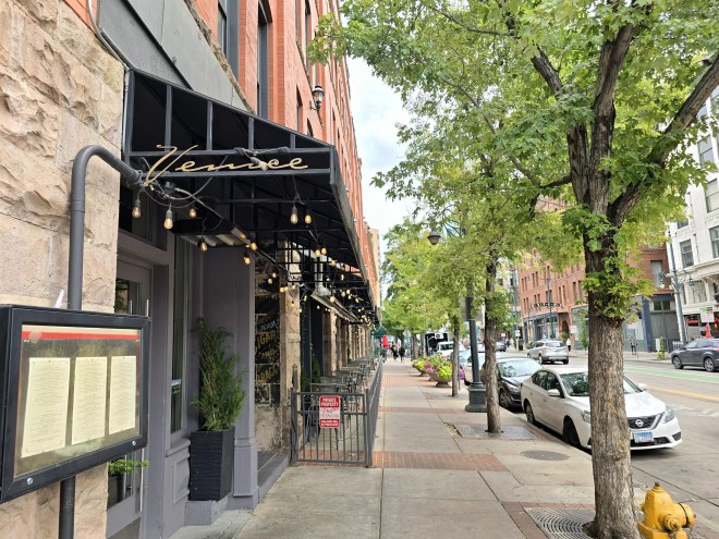 black awning on building next to a sidewalk lined with trees