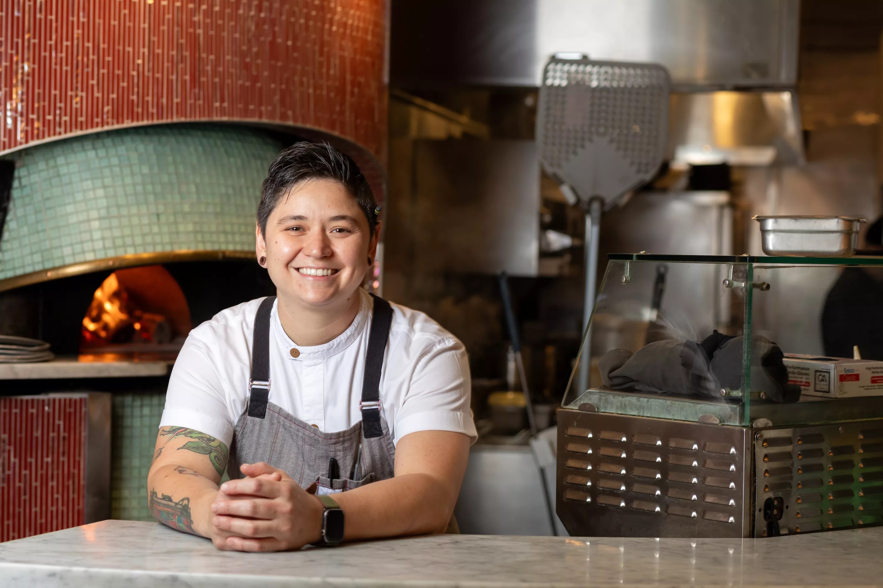 person in an apron posing by a good fired oven
