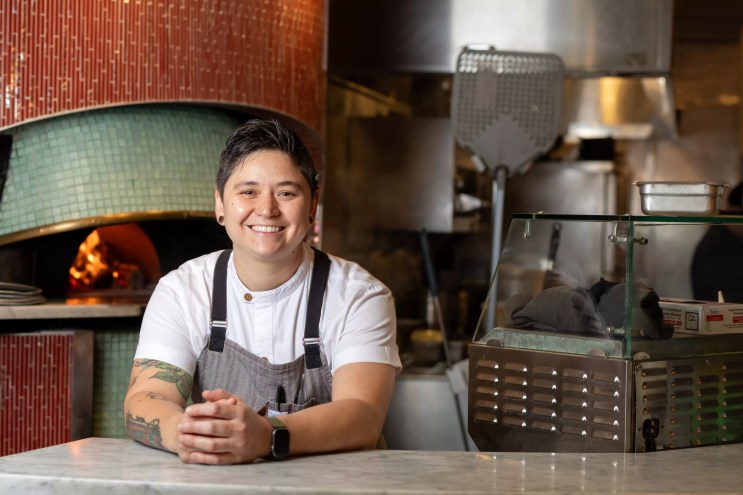 person in an apron posing by a good fired oven