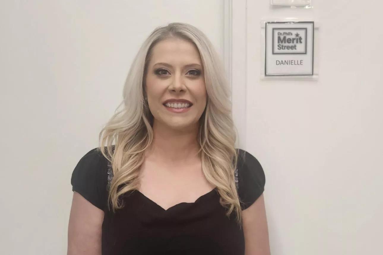 A woman stands in front of a door smiling.