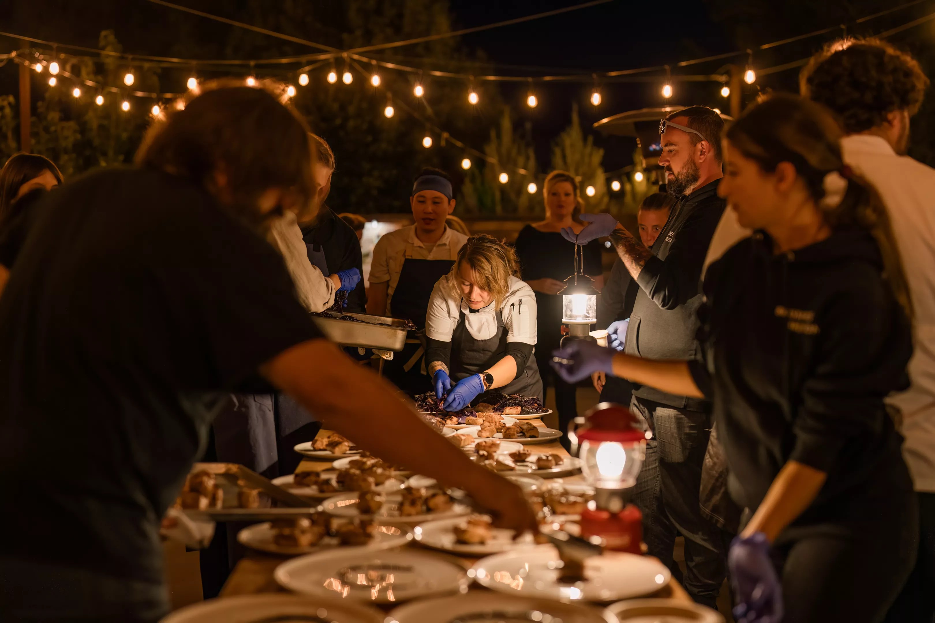 Several chefs around a dimly-lit table, plating a course during Harvest Week
