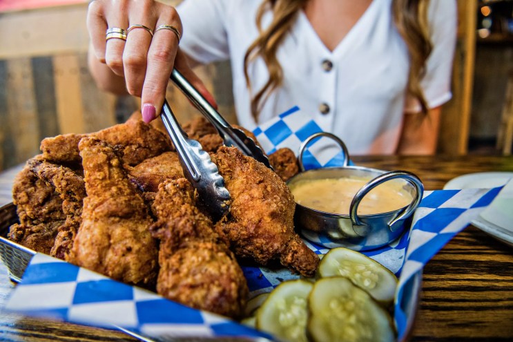 A woman using tongs to pick up fried chicken