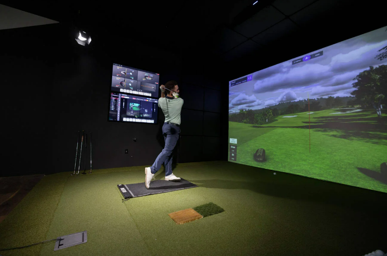 Man swings golf clubs in indoor golf simulator