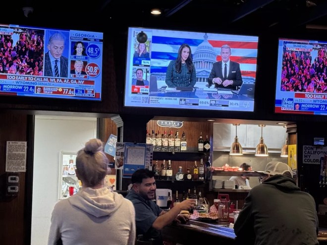 A woman watches TV at a bar.