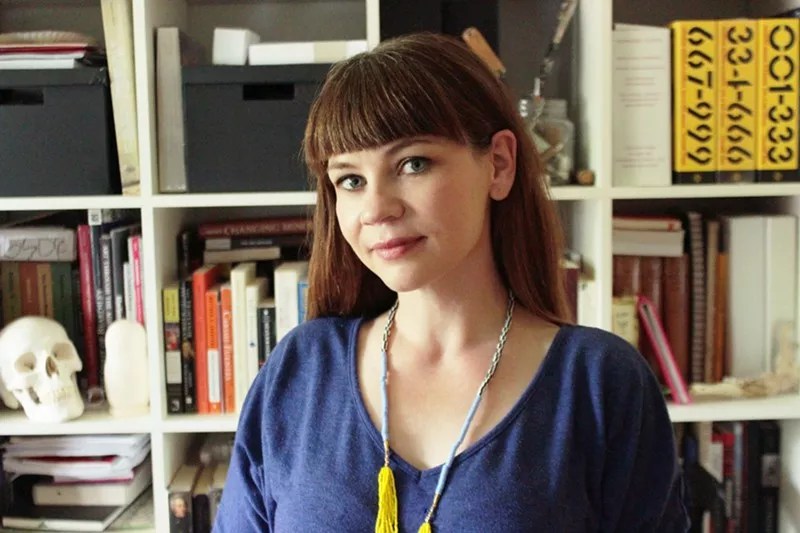 woman in blue dress standing in front of a bookshelf