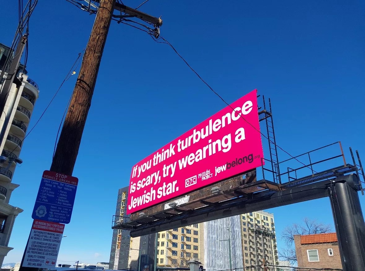 A pink billboard reads, “If you think turbulence is scary, try wearing a Jewish star.”