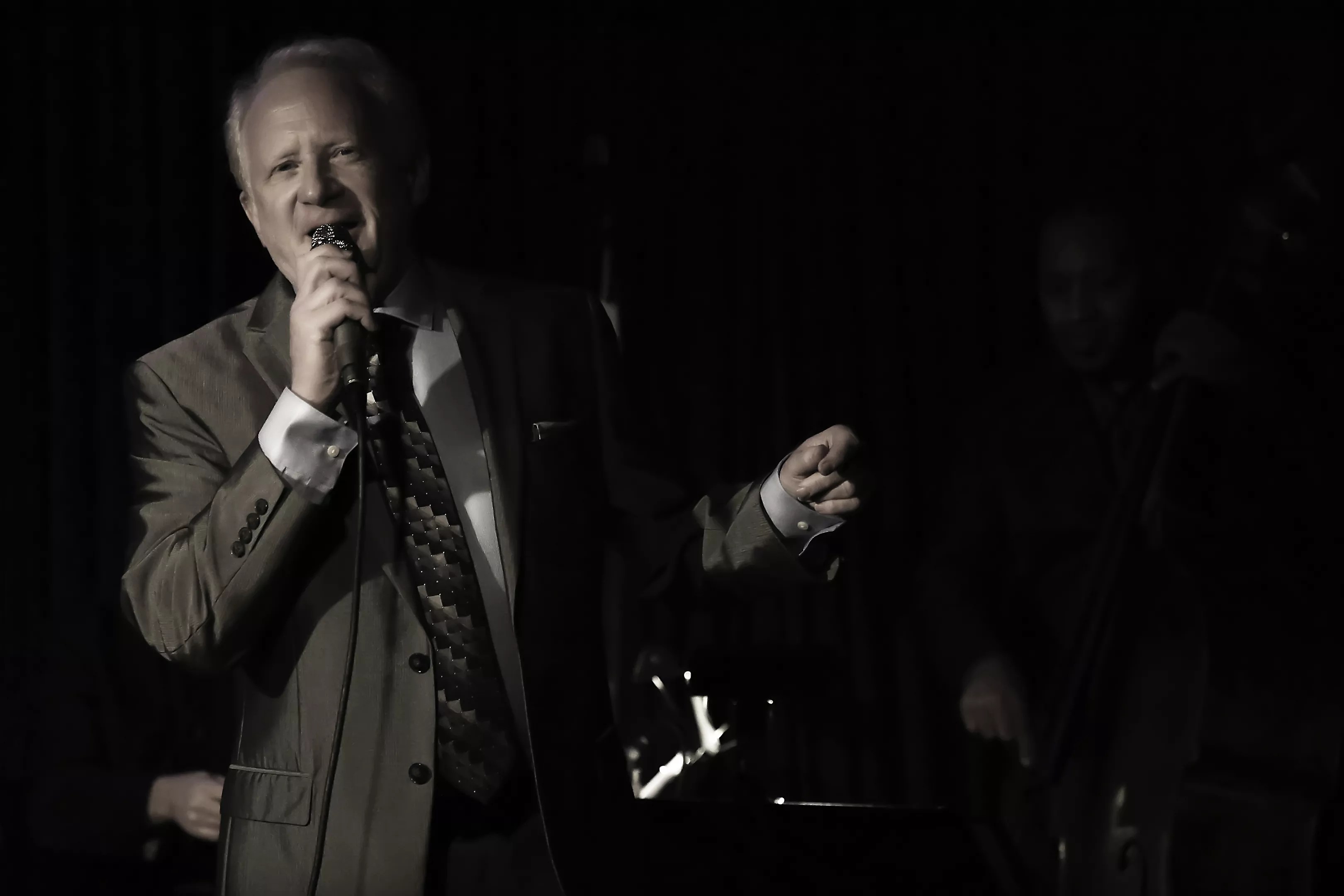 A man in a suit sings with a microphone on stage.