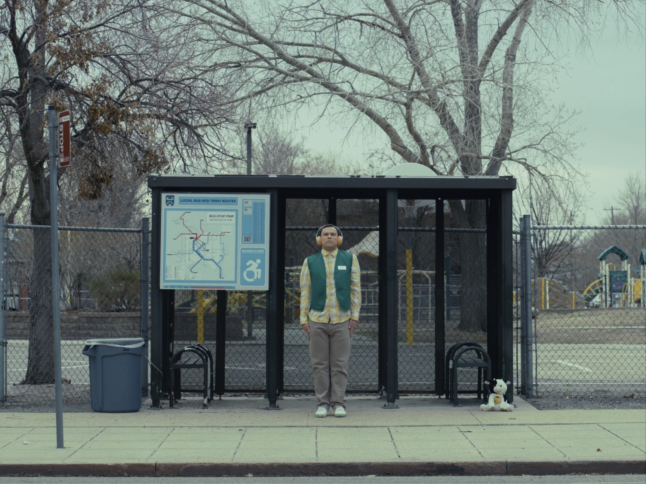 Man with headphones stands at a bus stop.