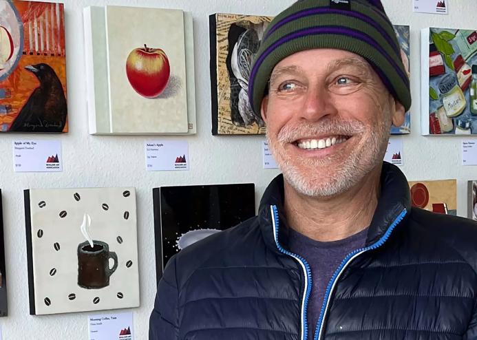 artist in hat in front of paintings