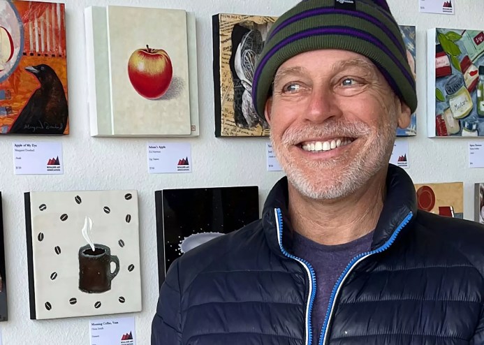 artist in hat in front of paintings