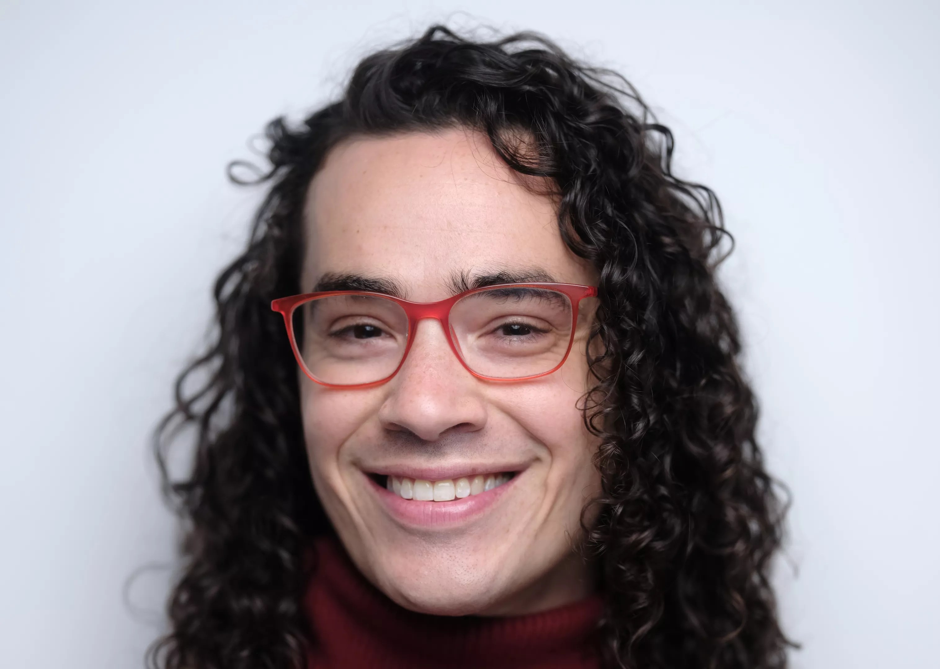 Headshot of a curly haired man in pink glasses.