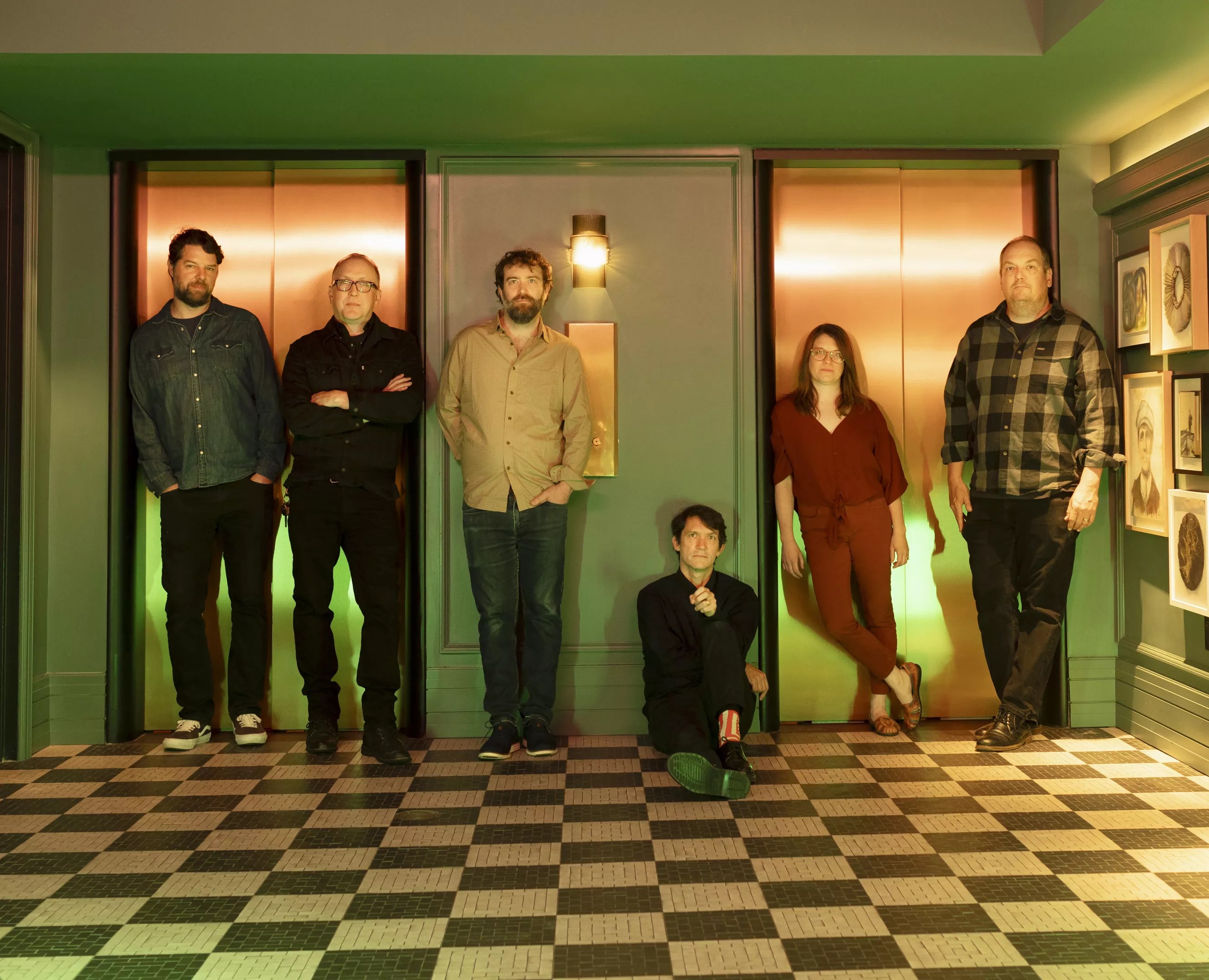The members of the band Cursive in a hotel's elevator bay, all standing except songwriter, guitarist and vocalist Tim Kasher.