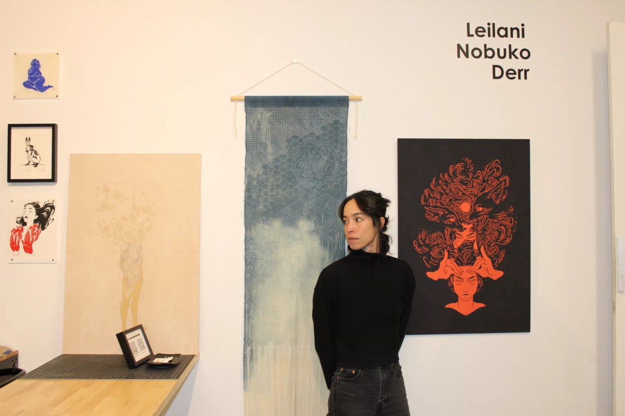 A woman poses in her studio in front of her artwork.