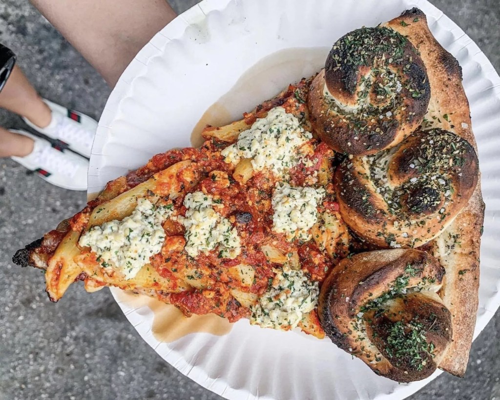 A thick slice from Mora Pizza topped with pasta and vegan cheese