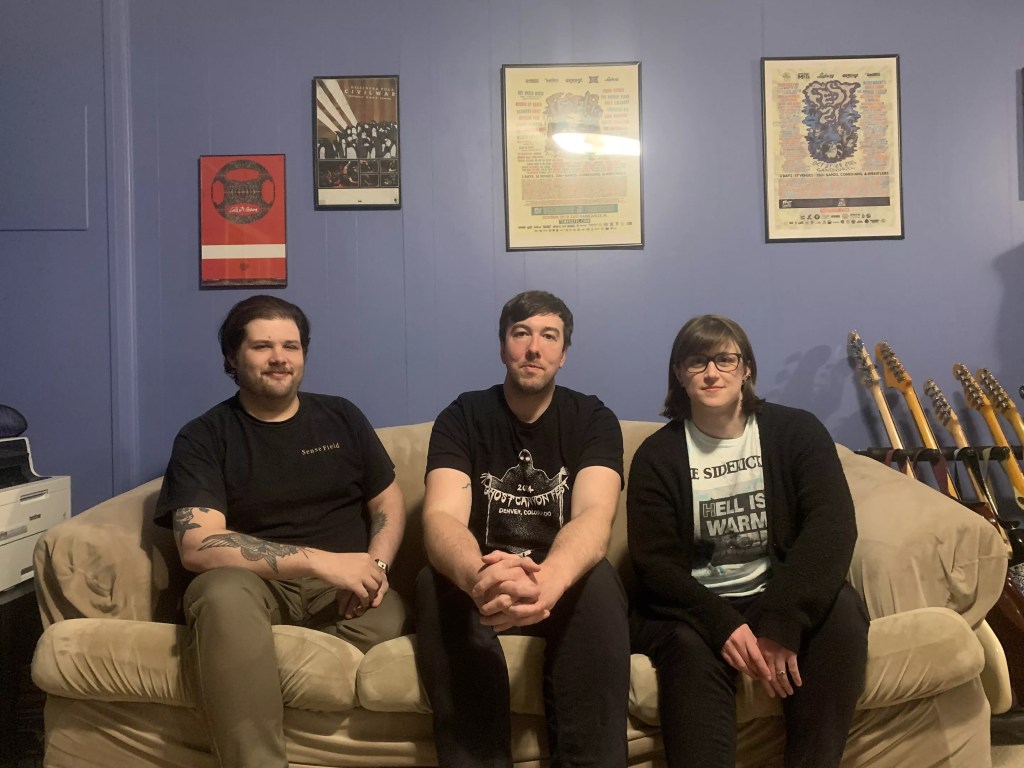 The three members of Power Goth Recordings sitting on a couch in their basement home studio.