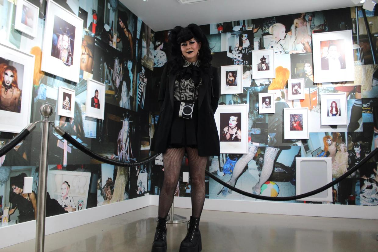 A woman dressed in black stands in front of a wall of photos