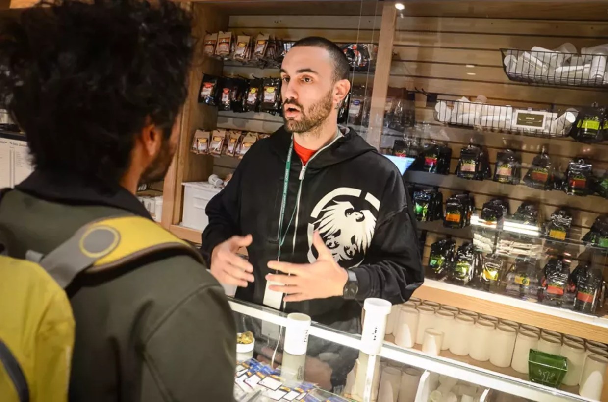 Dispensary budtender assists customer with marijuana purchase