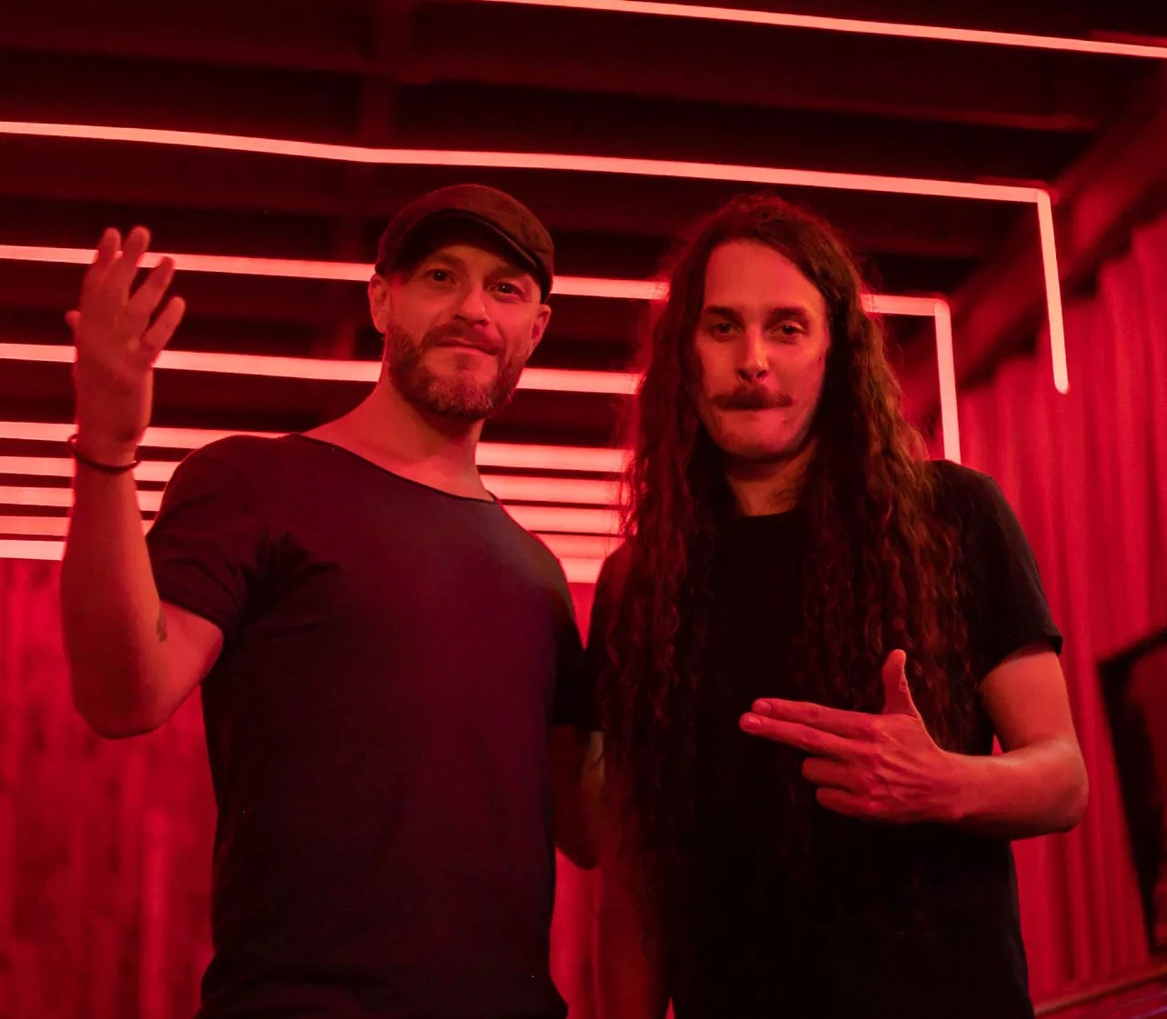 Two men pose in a room with red lights.