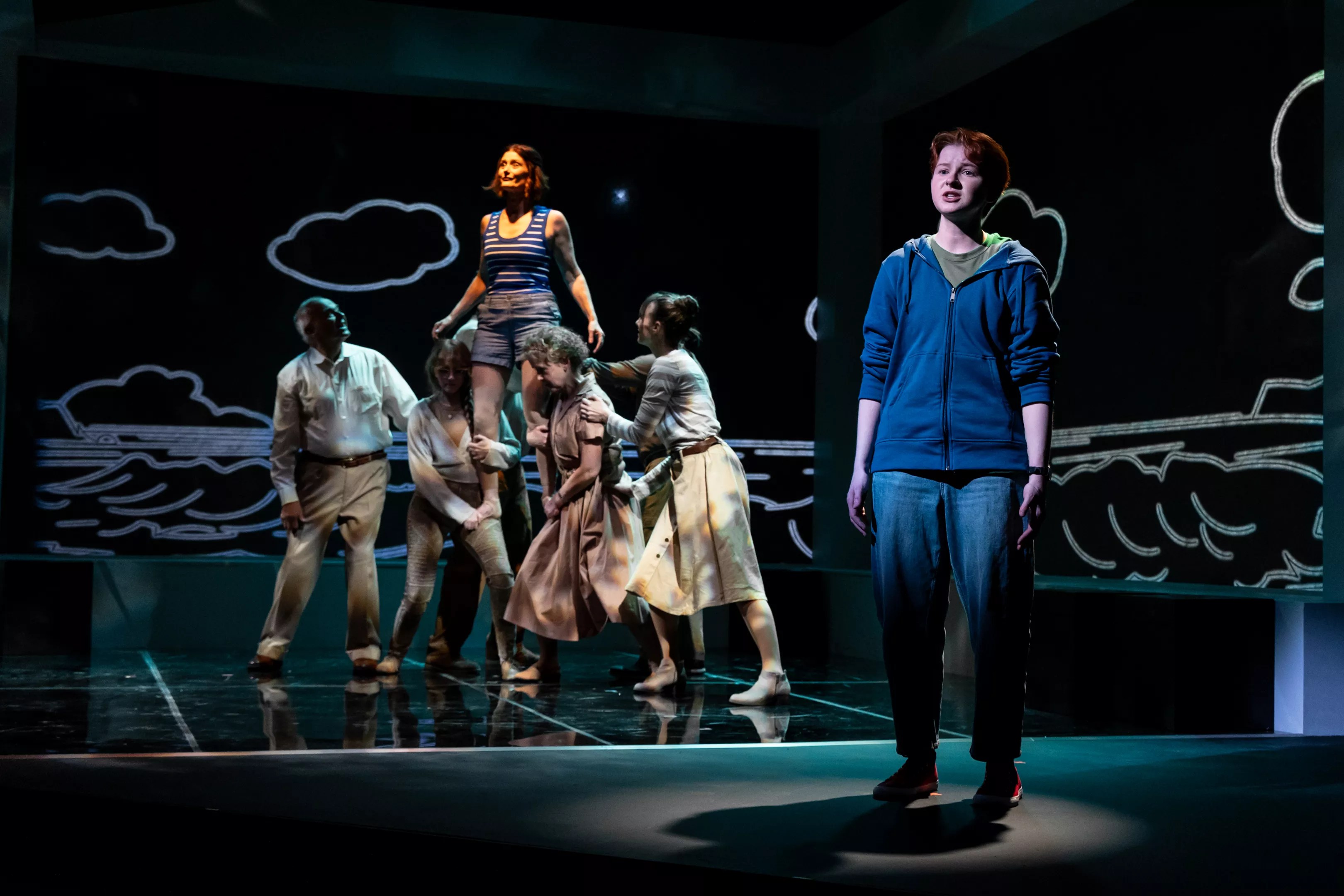 A boy stands while a woman is raised by a crowd behind him.