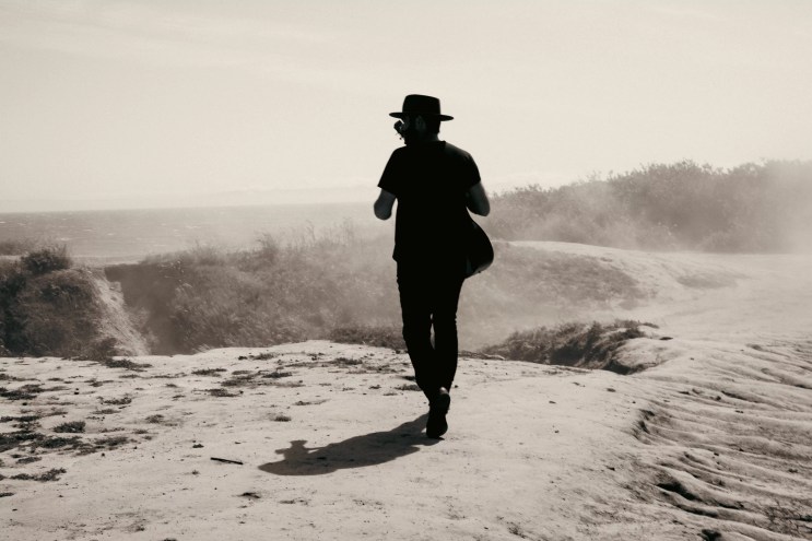 man walking around plains with a guitar strapped on his back