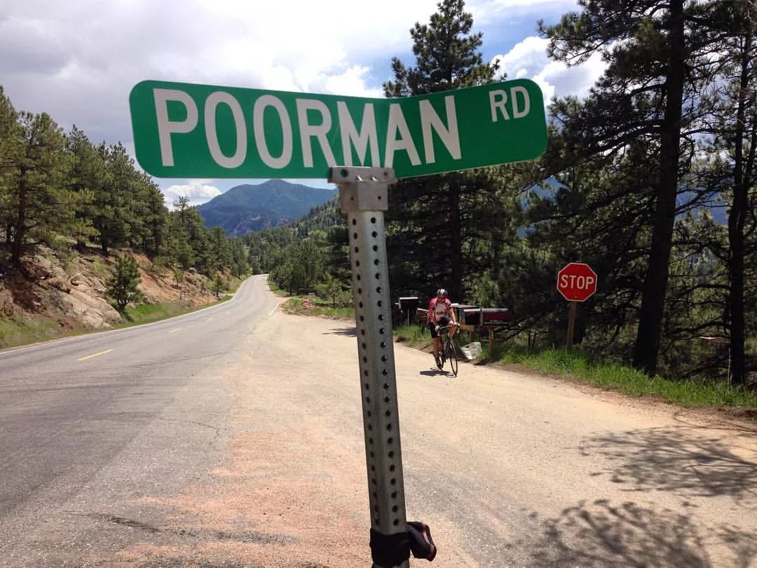 A man rides a bike near a sign that reads Poorman