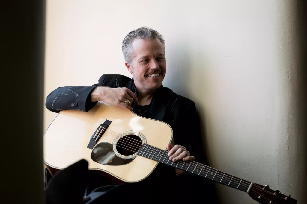 Jason Isbell smiles while holding a guitar