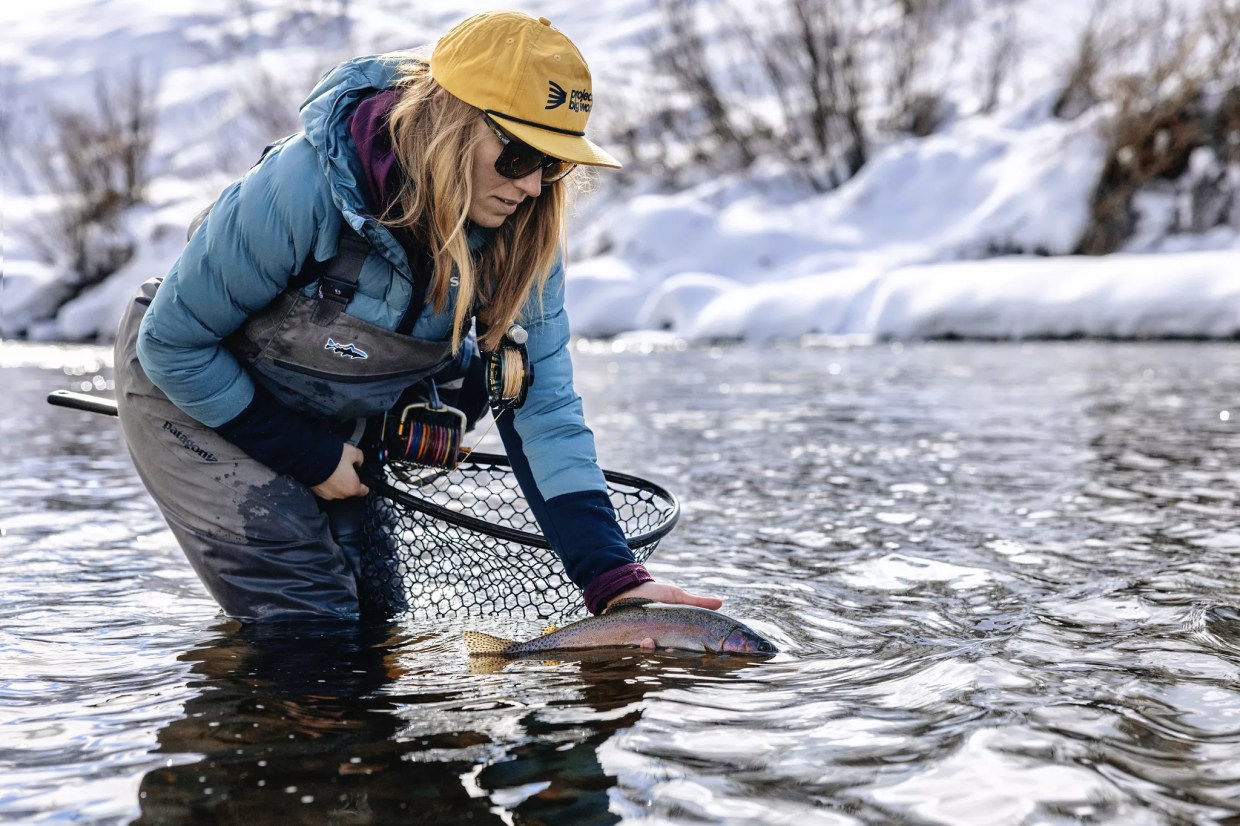 A female fly fishing guide releasing a trout into a river