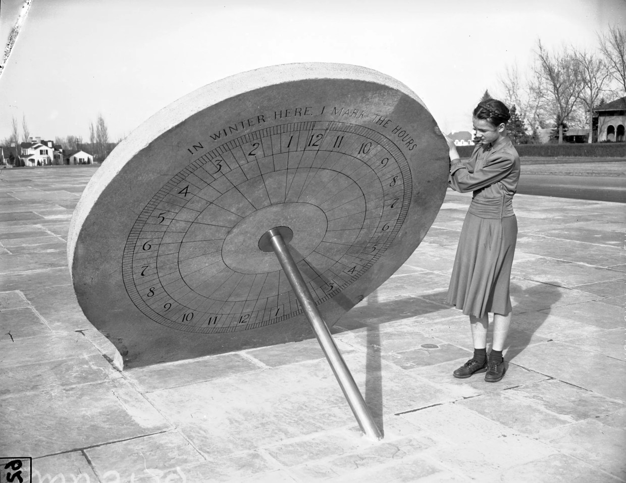 An old photo of a woman standing by a sundial