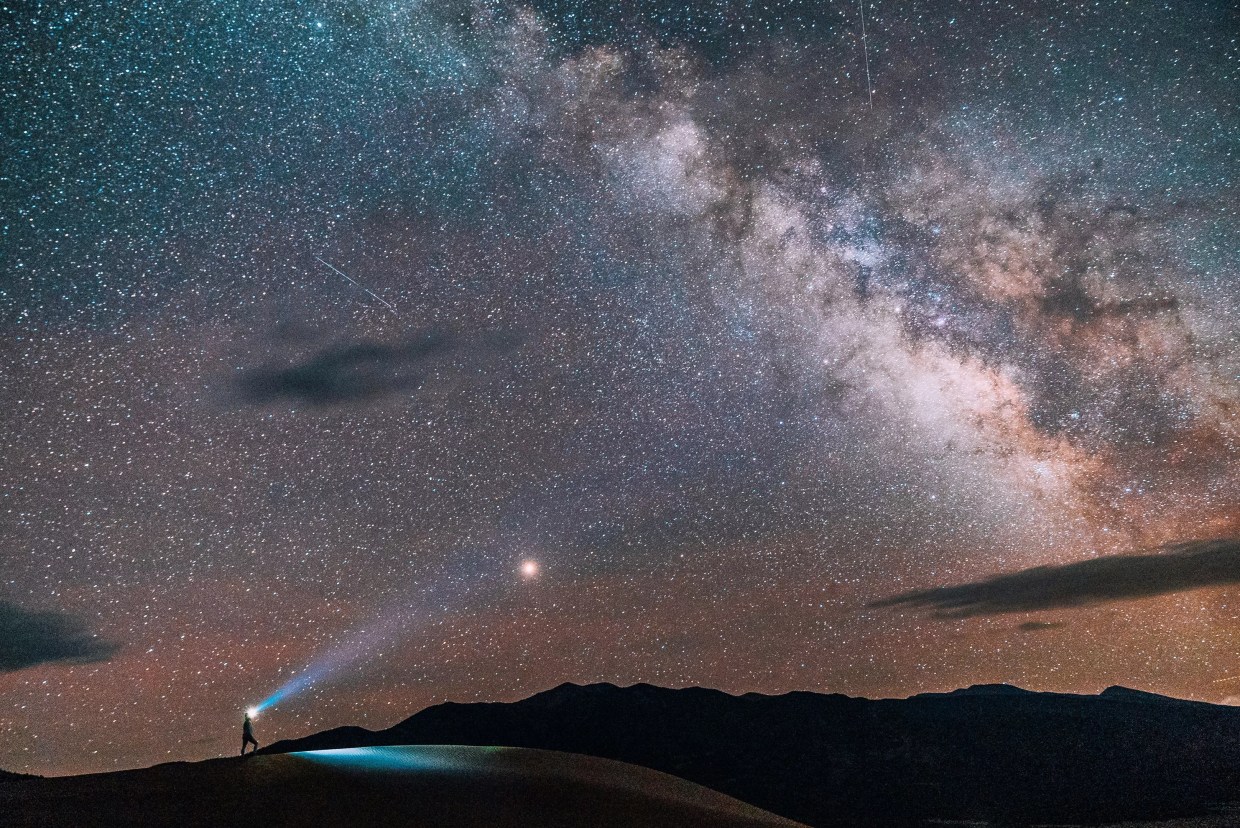 A person wearing a headlamp while hiking beneath the Milky Way at Great Sand Dunes National Park