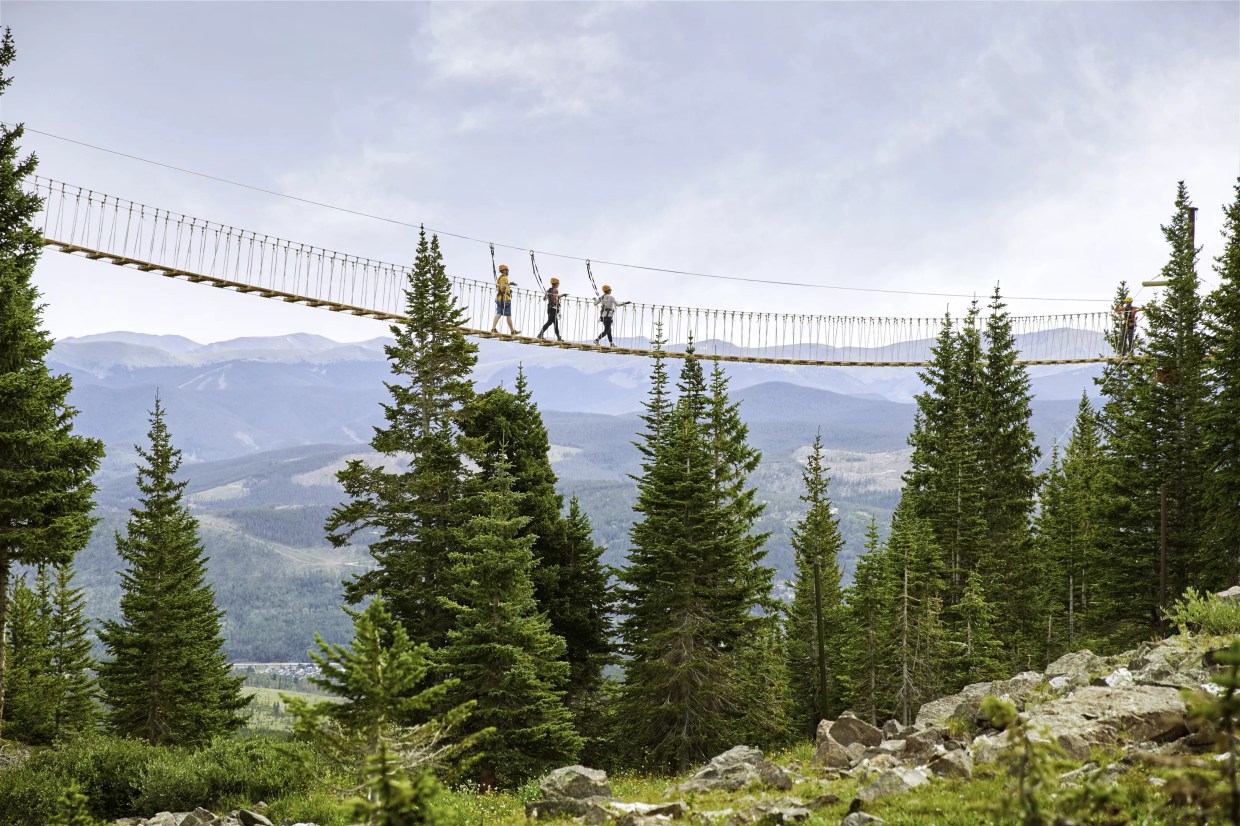 Three people backdropped by mountains while crossing the aerial bridge at Breckenridge Ski Resort