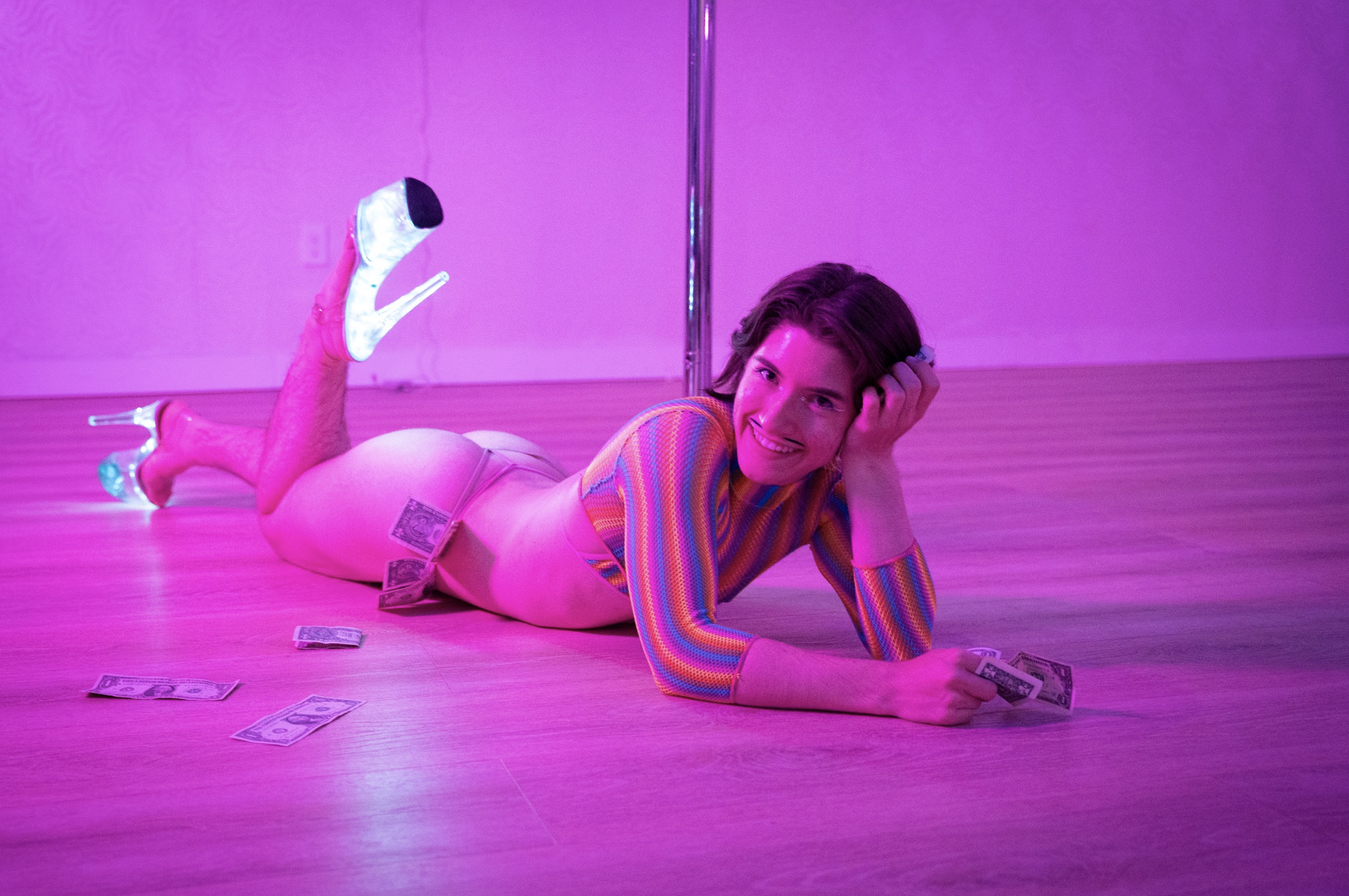 A pole dancer poses by a pole.