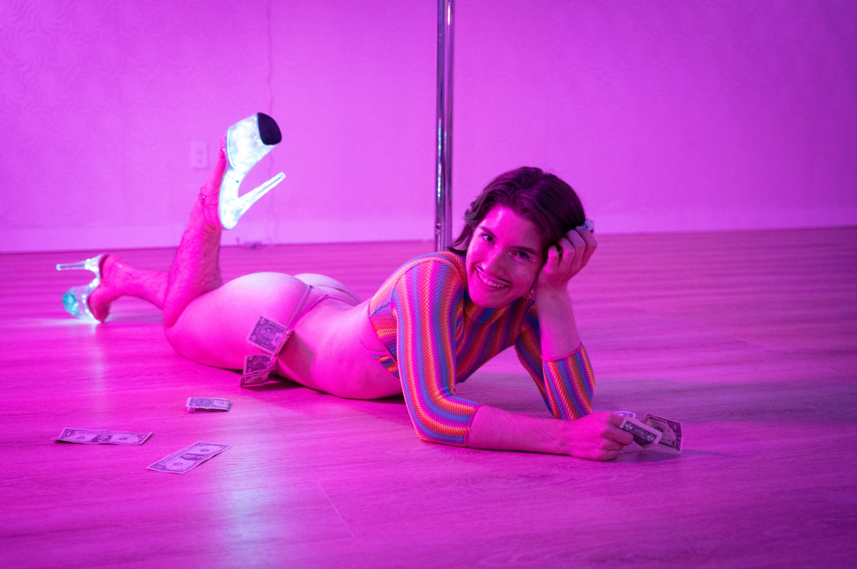 A pole dancer poses by a pole.