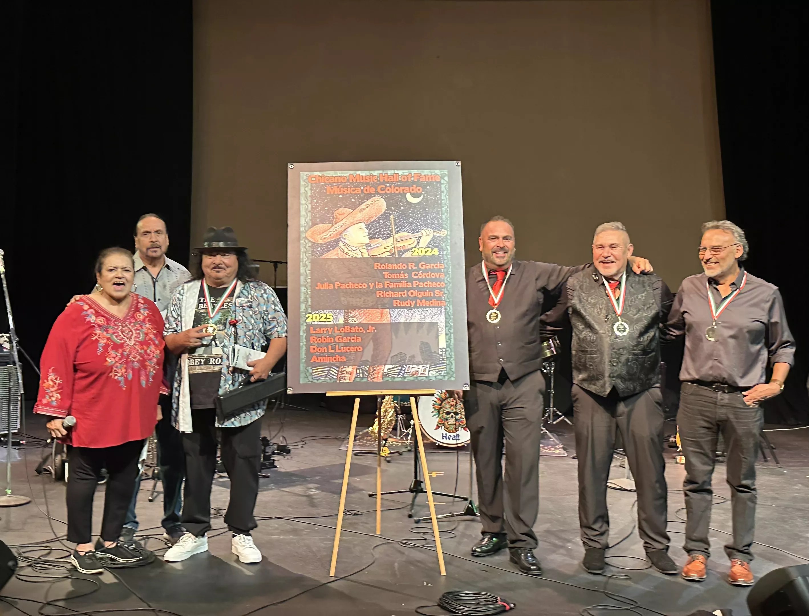 The four inductees of the Chicano Music Hall of Fame stand before a crowd on stage at Su Teatro Cultural & Performing Arts Center.