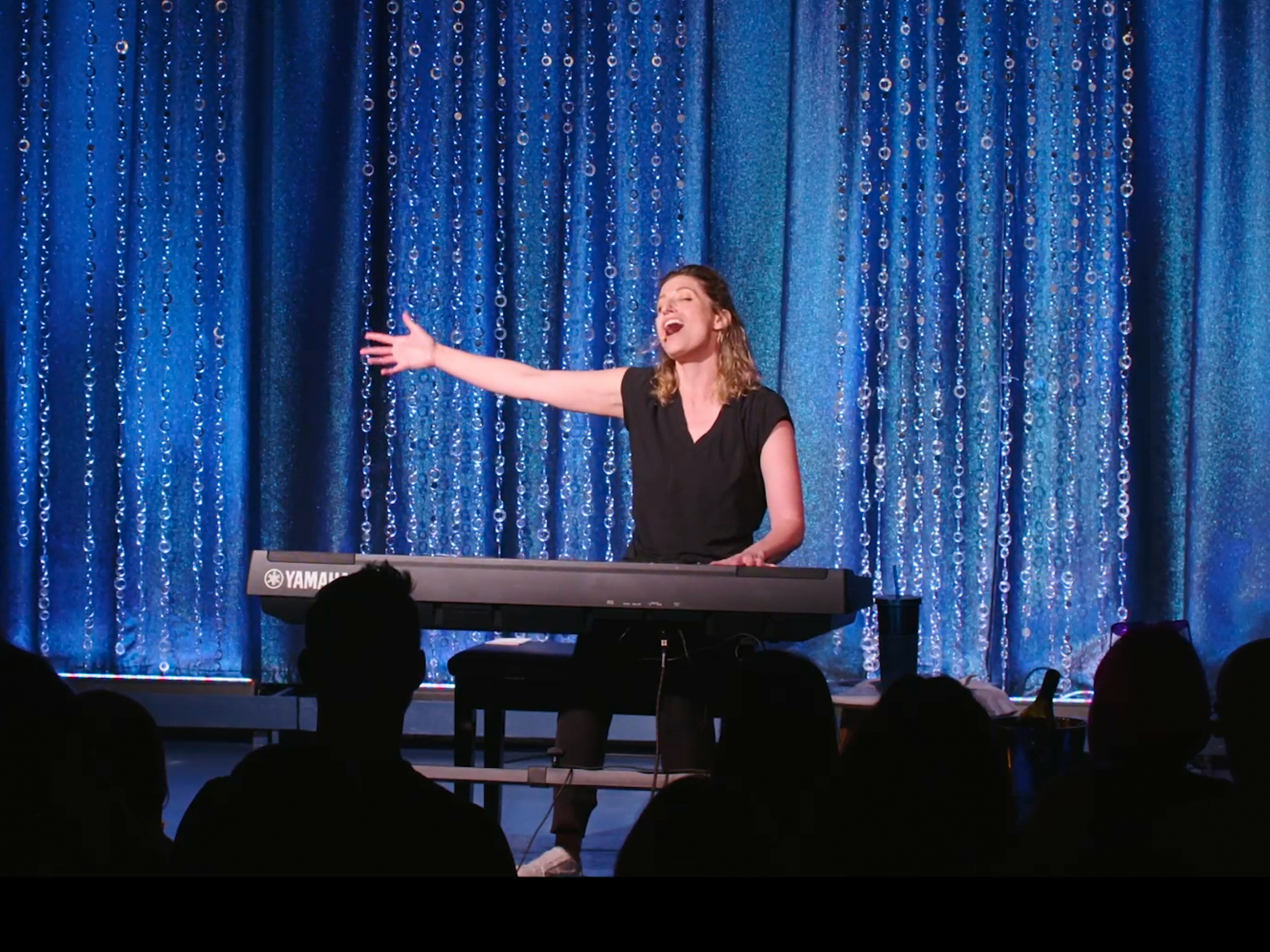 woman at piano in front of curtain.